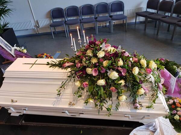 Weißer Sarg mit Blumenarrangement und Kerzen bei einer Trauerfeier in einer Kapelle.