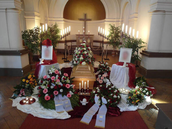 Trauerfeier in Kirche mit Sarg, Blumen, Kerzen und Gestecken zur Bestattung.